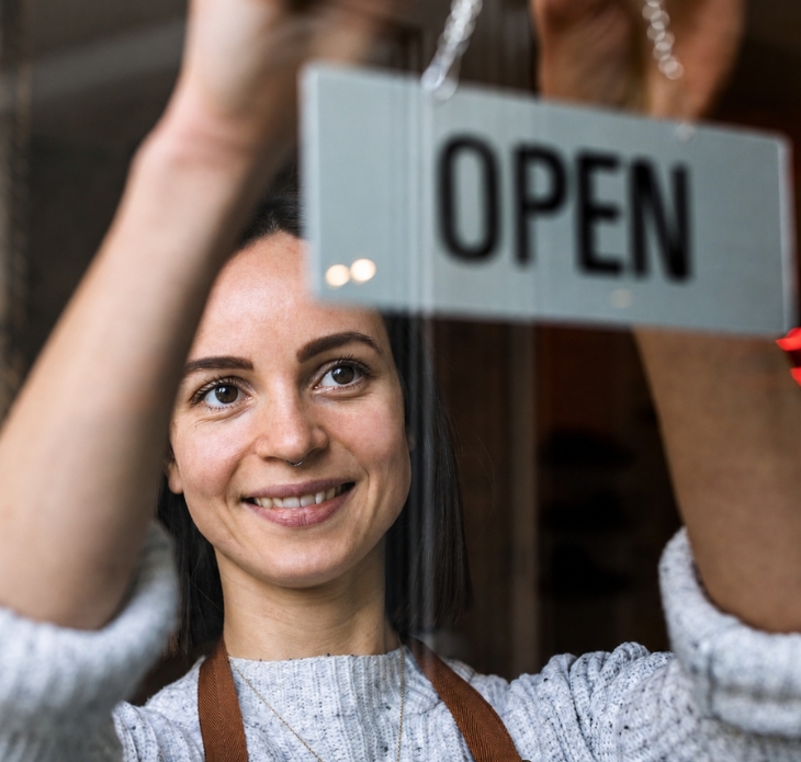 Uśmiechnięta właścicielka lokalu z tabliczką „OPEN”