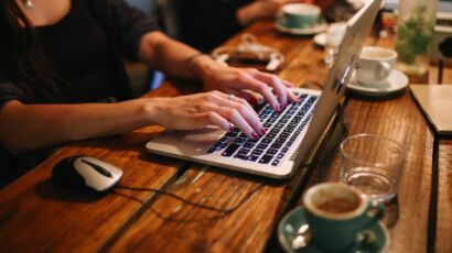 Osoba pracująca na laptopie przy filiżance kawy