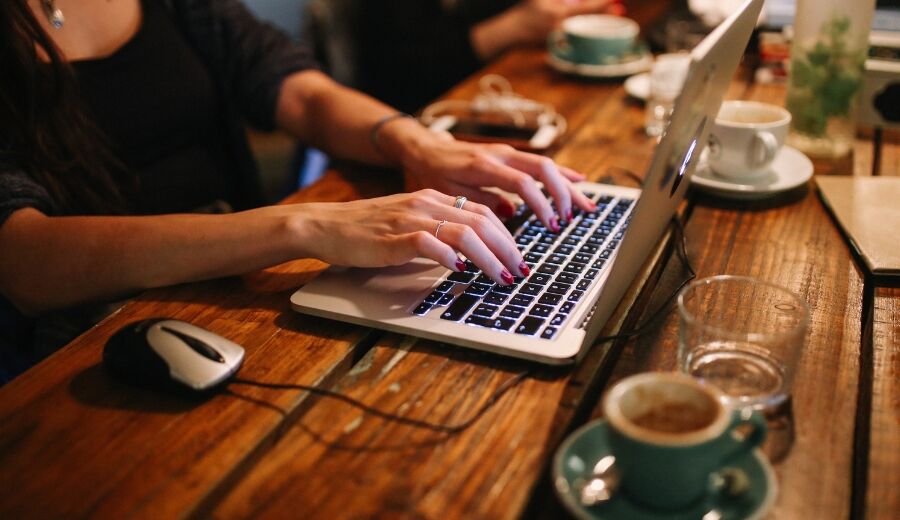 Osoba pracująca na laptopie przy filiżance kawy
